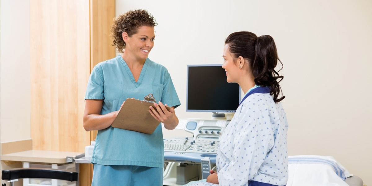 Health care worker talks with patient in hospital bed.