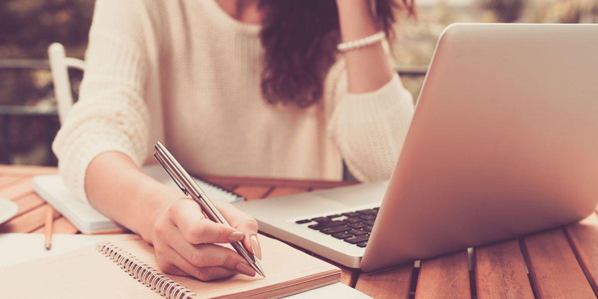 Female student looking at laptop and taking notes on paper.