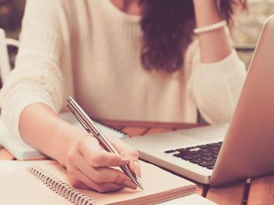 Female student looking at laptop and taking notes on paper.