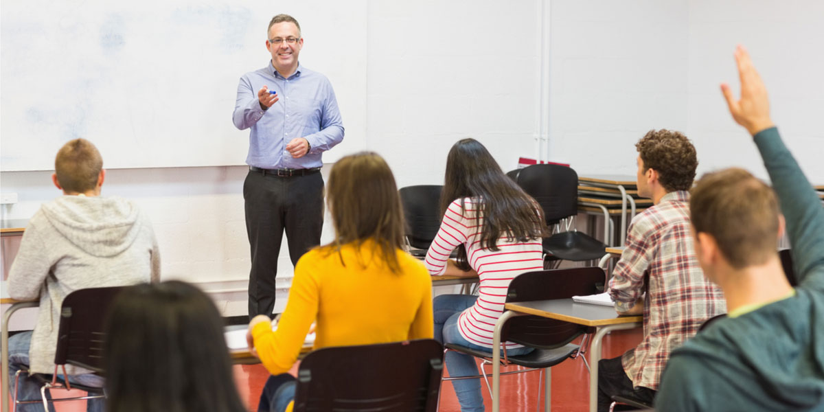 Male teacher stands in front of classroom.